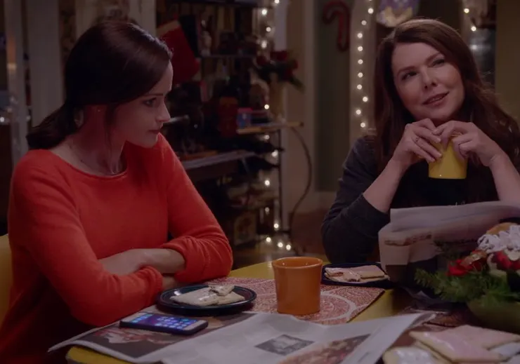"Lorelai and Rory Gilmore sitting in a cozy coffee shop, smiling and chatting"