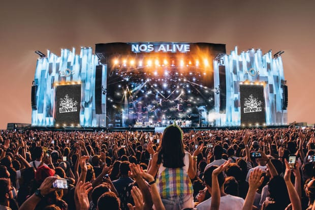 Festival crowd at NOS Alive in Lisbon with coastal backdrop and live rock music stage.