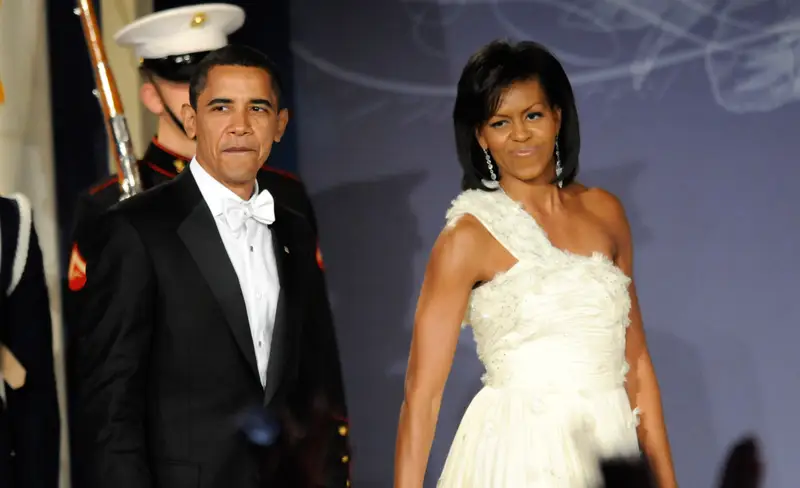 “Barack and Michelle Obama walking hand in hand, laughing together at a public event, representing teamwork and shared values.”