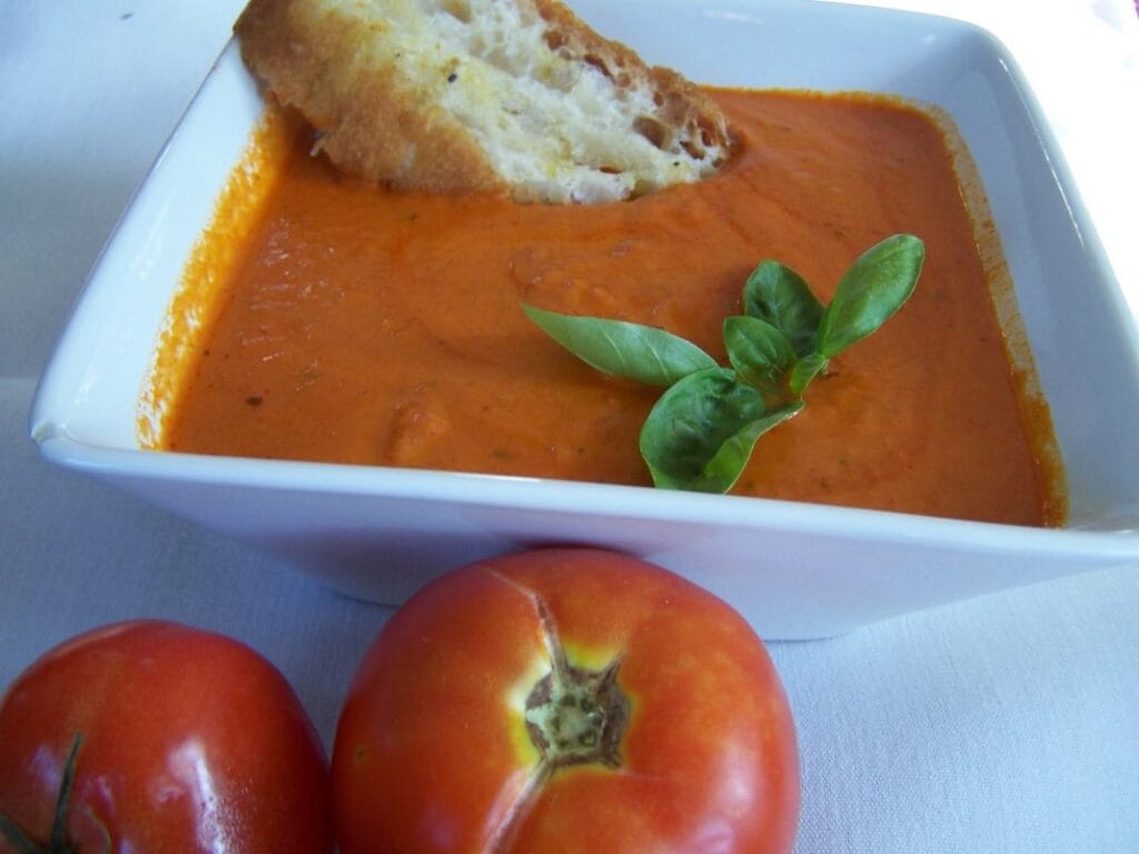 Smooth tomato soup in a white bowl, swirled with cream and topped with fresh basil leaves.