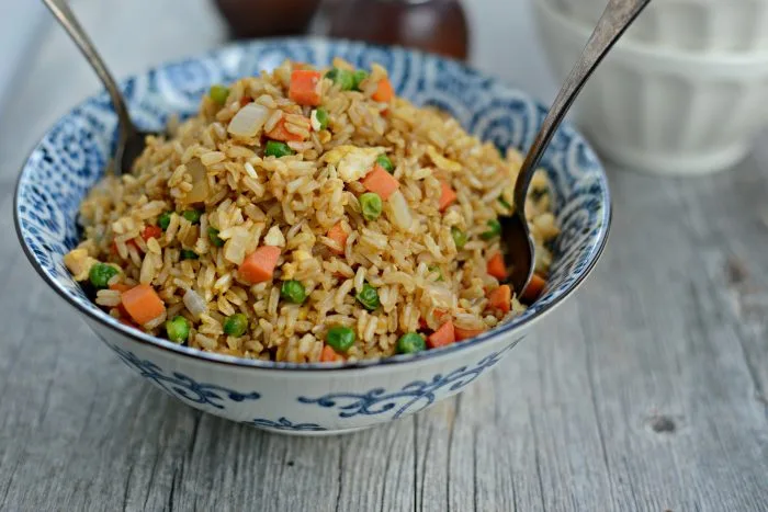 “Healthy egg fried rice made with brown rice, peas, and carrots in a wok.”
