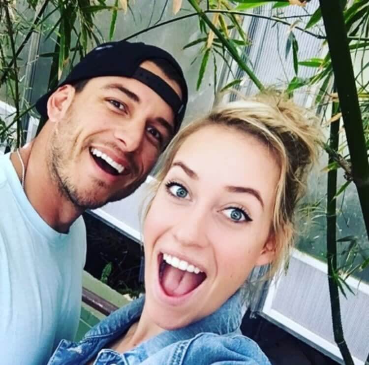 Paige Spiranac and fiancé Steven Tinoco smiling together at a golf event.