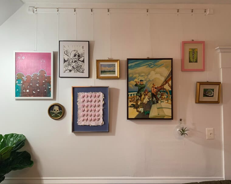 A row of picture frames hanging from a tension rod mounted between two walls, creating a damage-free gallery wall in a rental space.