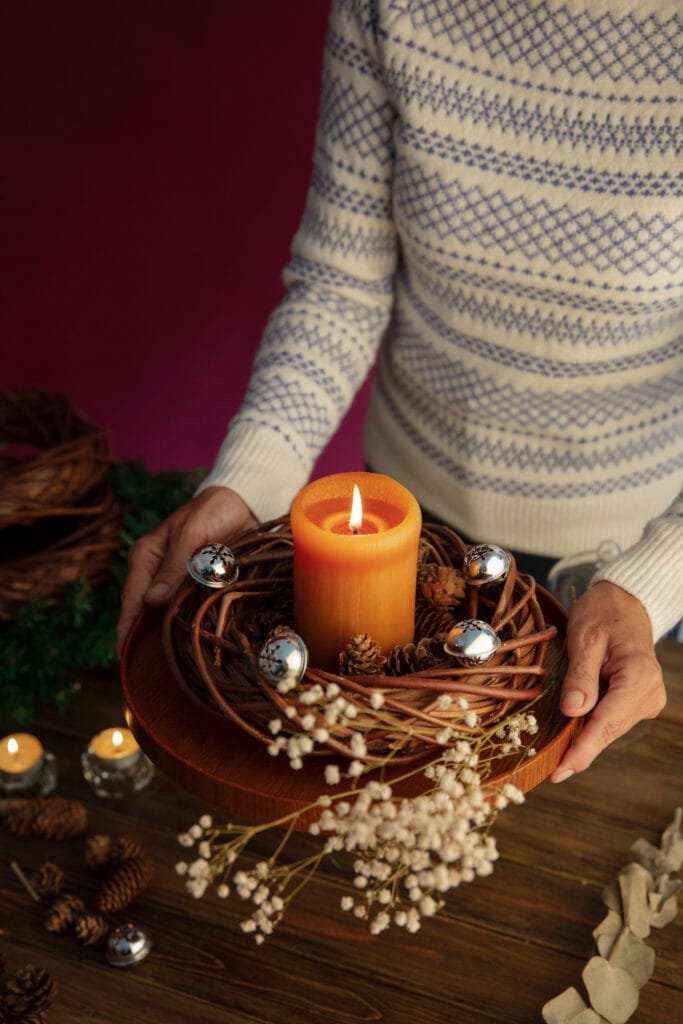 Woman lighting a festive holiday candle surrounded by pinecones and berries for a cozy Christmas scent.