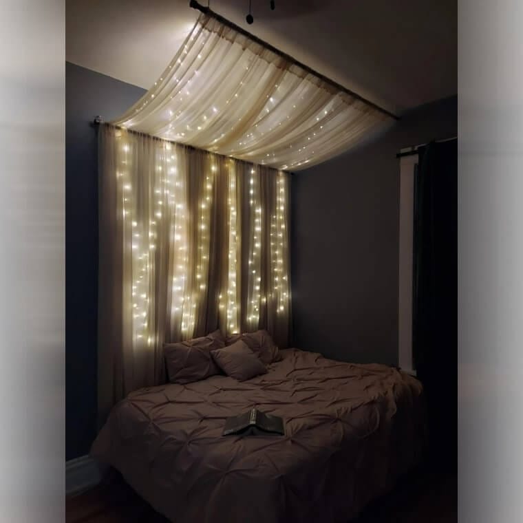 A DIY four-poster bed created by draping fabric over tension rods mounted above a bed for a dramatic, cozy effect.