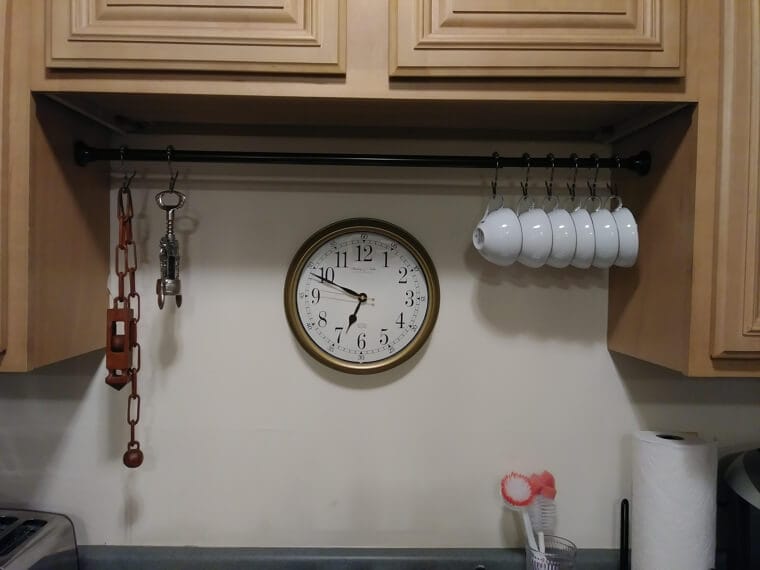 A cozy kitchen coffee station with mugs hanging from a tension rod, adding charm and easy access for daily coffee drinkers.