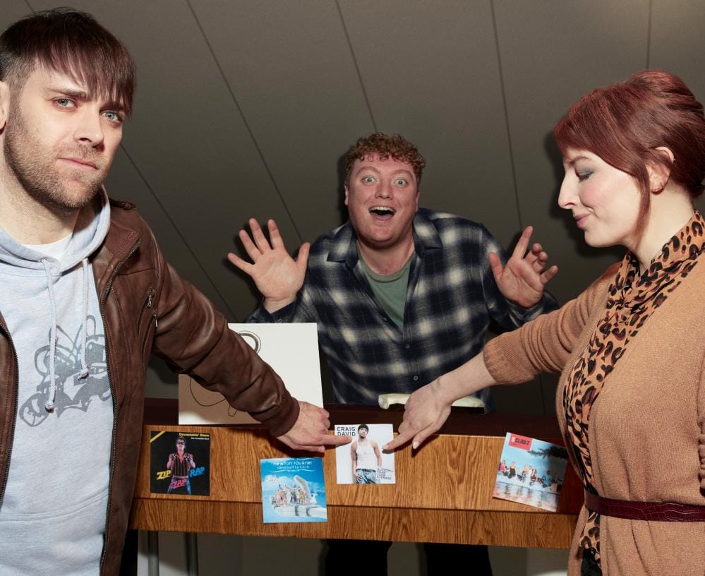 “Jamie Morton reading from his dad’s parody romance novel with friends laughing in studio.”