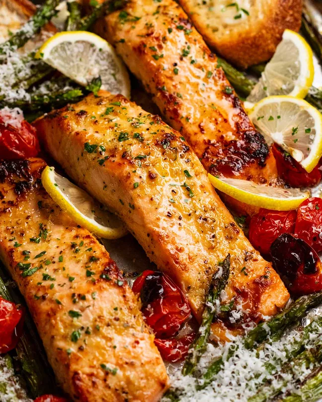 “Sheet pan with baked salmon fillets, broccoli, and zucchini drizzled with lemon and olive oil.”