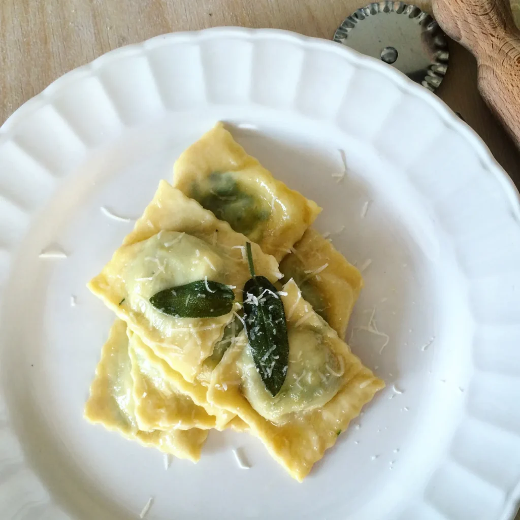 “Homemade ravioli stuffed with ricotta cheese and spinach, topped with butter and sage – elegant Italian pasta dish to prepare at home.”