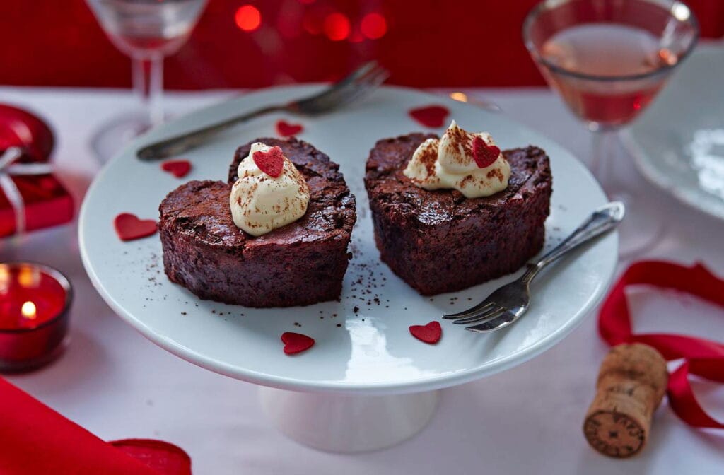 “Fudgy red velvet brownies cut into heart shapes and drizzled with cream cheese icing for Valentine’s Day”