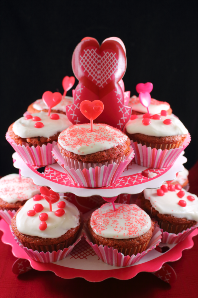 “Red velvet cupcakes with rose-shaped cream cheese frosting and heart sprinkles for Valentine’s Day”
