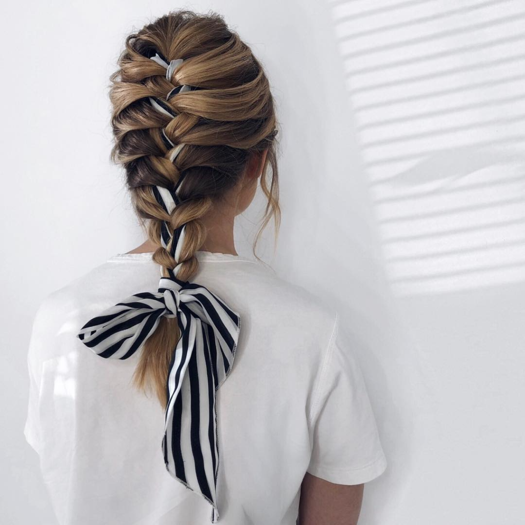 Woman wearing a colorful silk scarf as a headband over a bun, adding style and control in humid conditions — Best Hairstyles to Beat Summer Humidity.