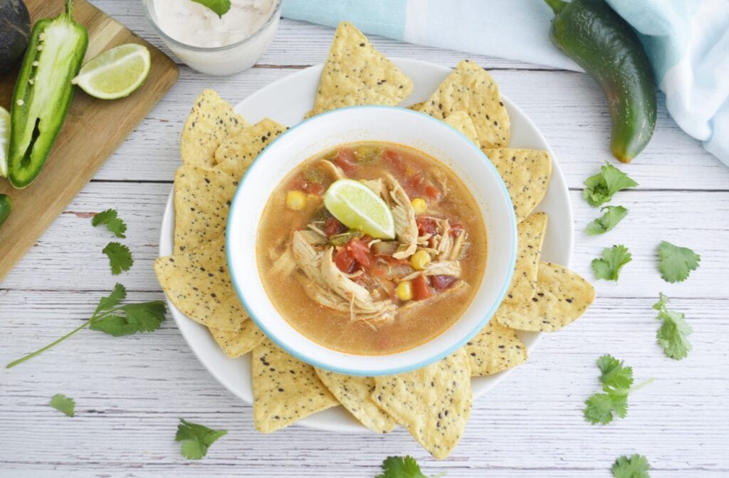 Colorful tortilla soup with shredded chicken, corn, black beans, and crispy tortilla strips on top.