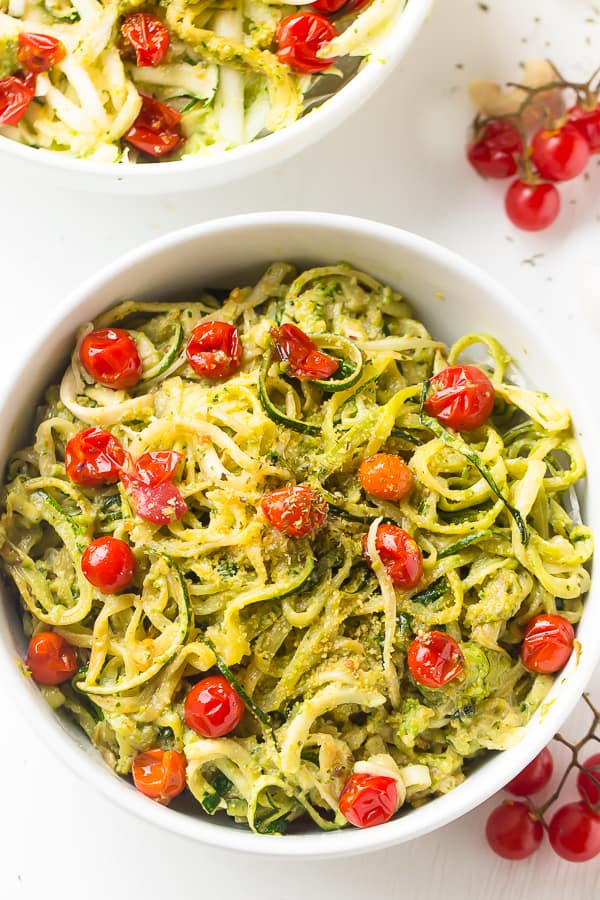 “Zucchini noodles tossed with green pesto and cherry tomatoes in a white bowl.”