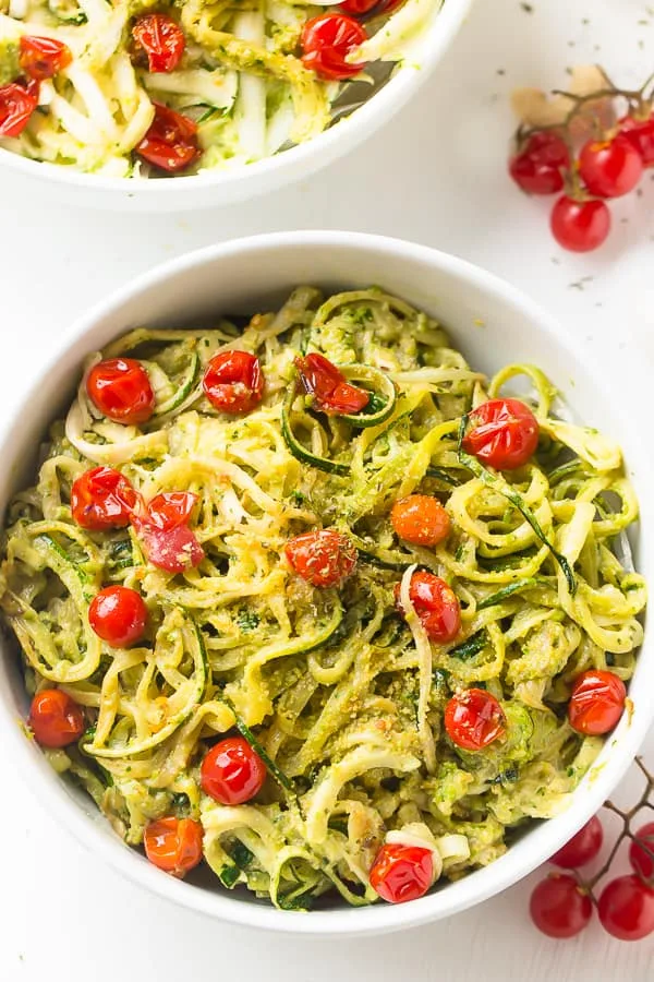 “Zucchini noodles tossed with green pesto and cherry tomatoes in a white bowl.”