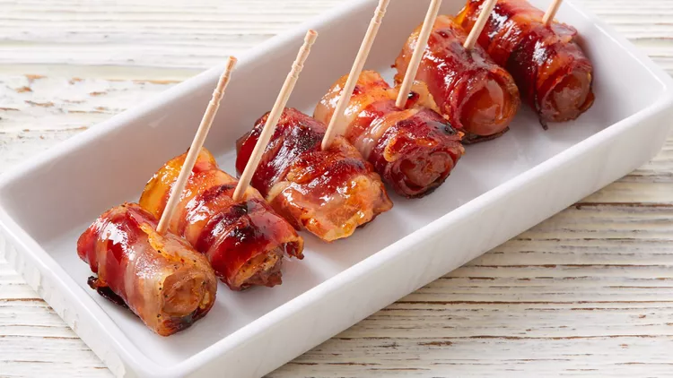 “Crispy bacon-wrapped dates stuffed with creamy goat cheese on a serving tray.”