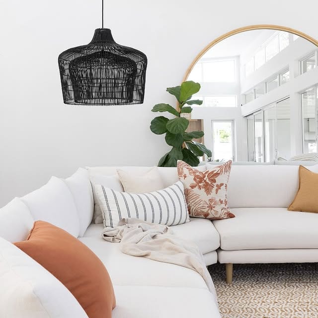 Modern living room with a black rattan pendant light contrasting white walls, light sofa, and warm terracotta accents.