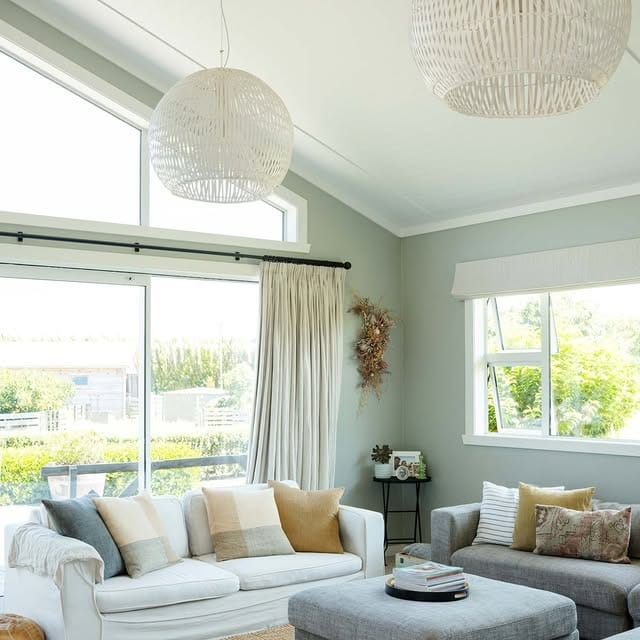 Cozy living room with oversized white rattan pendant lights, neutral color palette, jute rug, and tall windows.