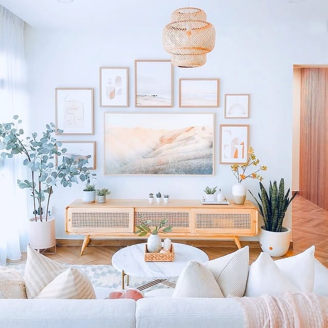 Soft coastal living room featuring a tiered rattan pendant light, pastel gallery wall, cane sideboard, and indoor plants.