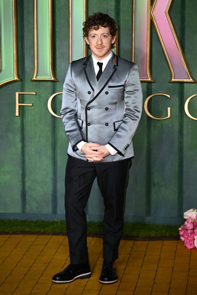 Ethan Slater in a metallic silver suit posing on the red carpet at the Wicked: For Good London premiere.