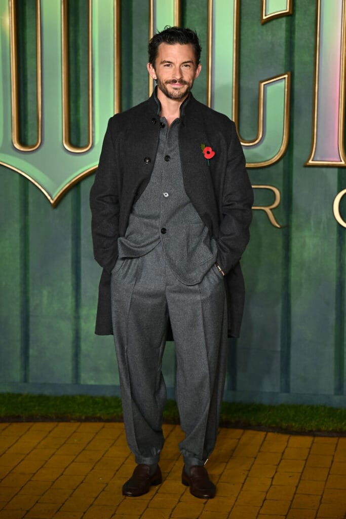 Jonathan Bailey wearing a gray wool suit with a red Remembrance Day flower at the Wicked: For Good London premiere.