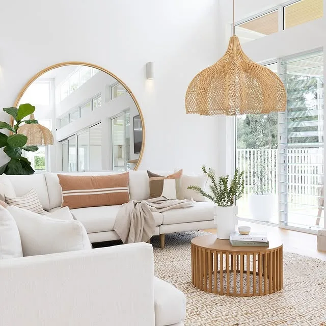 Neutral living room with a scalloped rattan pendant light, wooden coffee table, and large round mirror reflecting soft natural light.