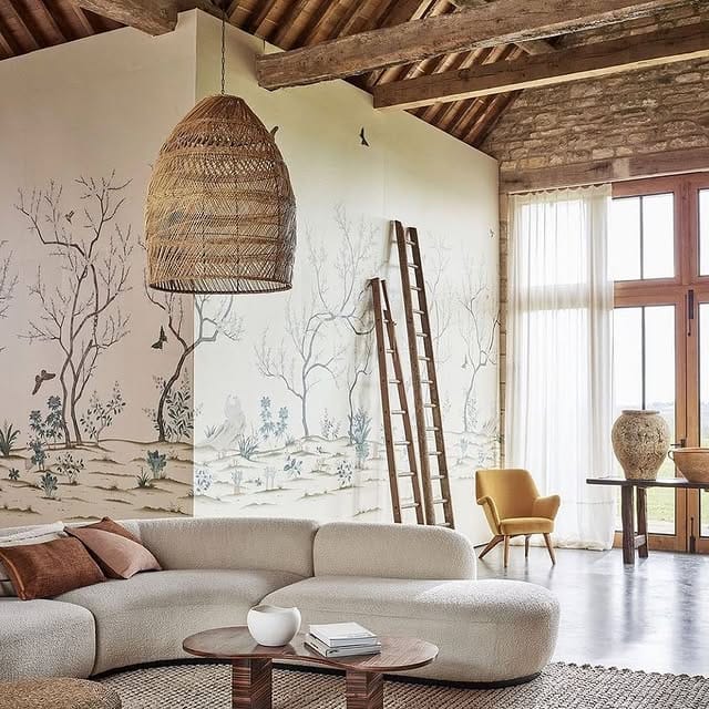 Rustic living room with a large rattan pendant light hanging from exposed wooden beams above stone walls and a curved sofa.