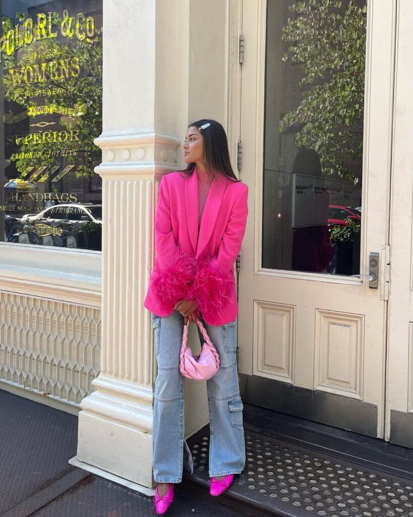 Hot pink feather-trimmed blazer paired with cargo jeans, pink heels, and a braided handbag for a trendy Valentine’s Day glam look.