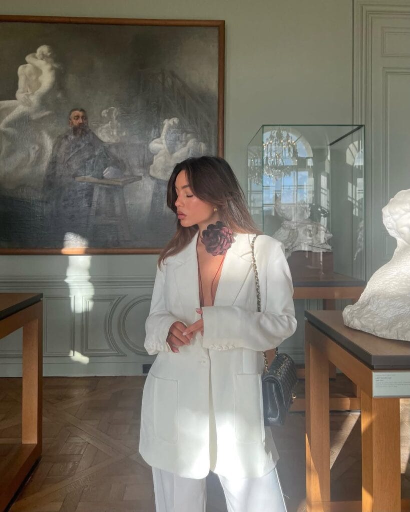 A white tailored blazer and wide-leg trousers paired with a deep-neckline floral tattoo-style top and a black quilted handbag for a minimalist Valentine’s look.