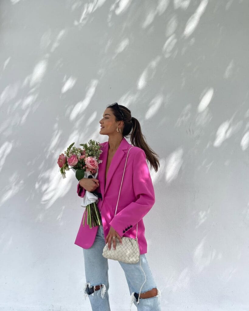 Hot pink blazer paired with distressed denim jeans, white quilted crossbody bag, and pink roses for a relaxed Valentine’s Day outfit.