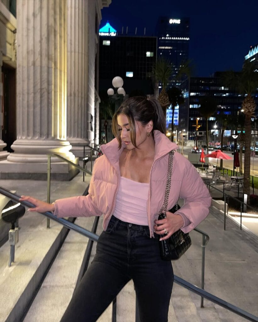 Blush pink cropped puffer jacket paired with a pink ruched tank top, black skinny jeans, and a black quilted shoulder bag.