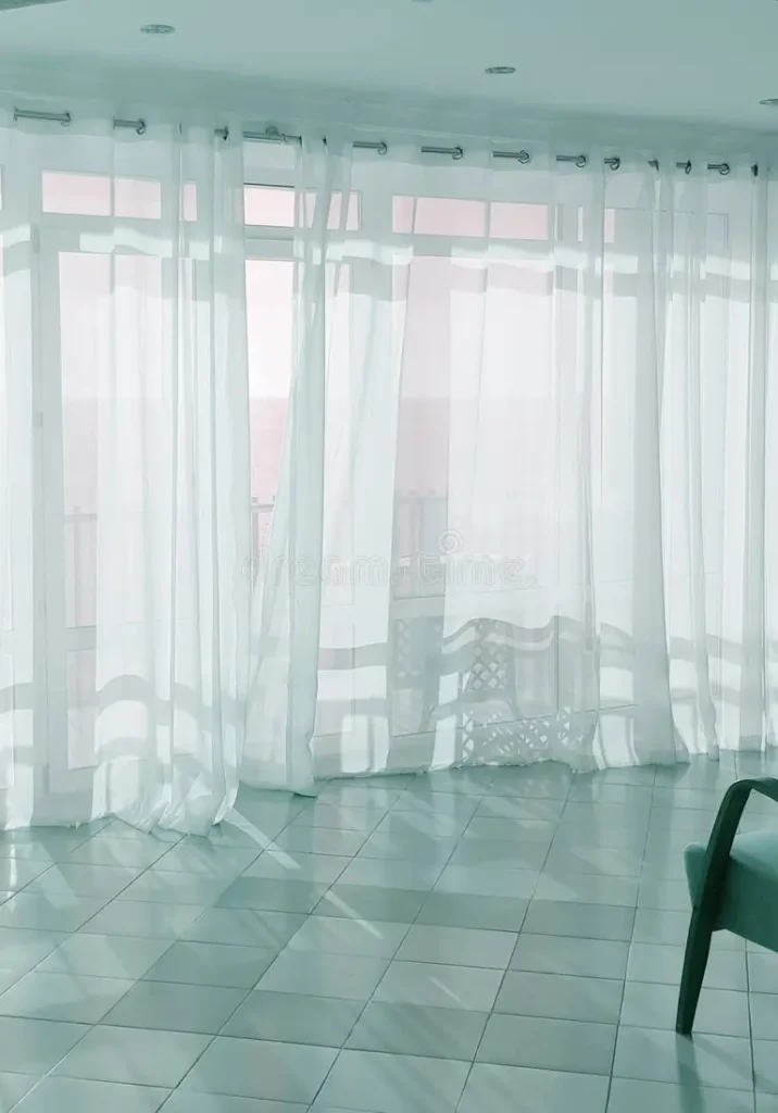 White sheer curtains hanging in a bright modern living room with natural sunlight.