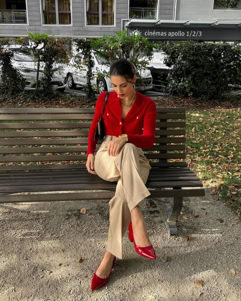 A fitted red cardigan with gold buttons styled with beige trousers, red heels, and a matching red handbag for a classic Valentine’s outfit.