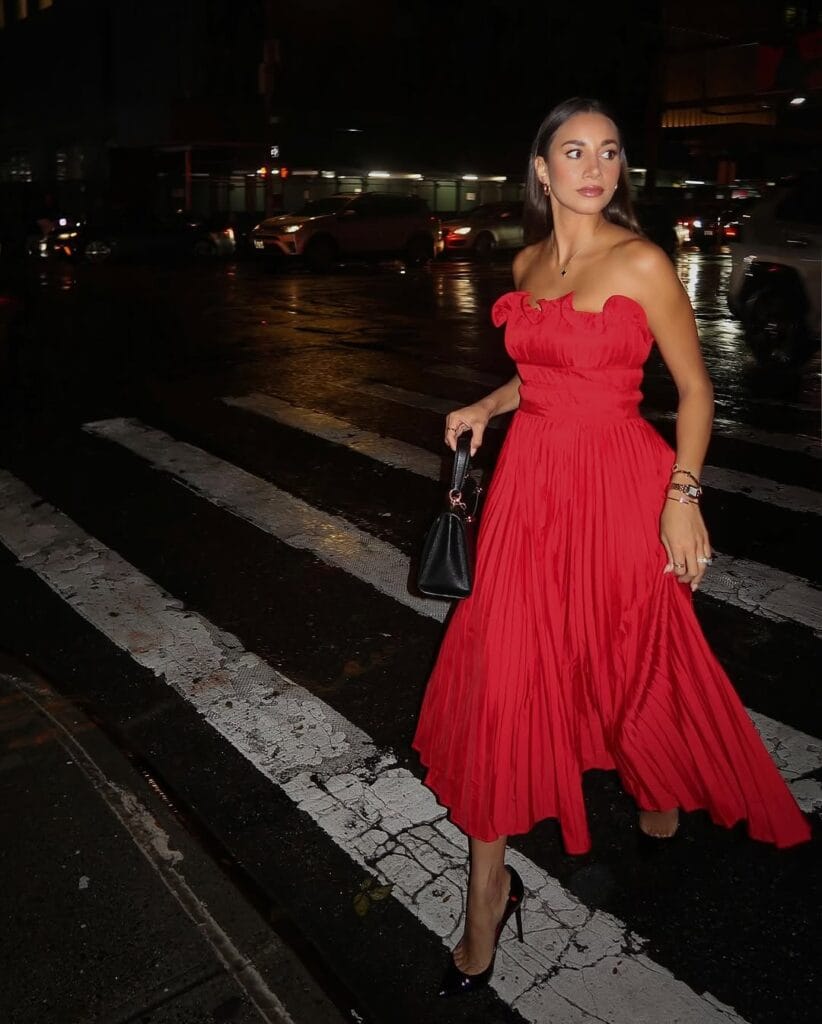 Red strapless midi dress with a pleated skirt, styled with black heels and a structured black handbag for a romantic Valentine’s evening look.