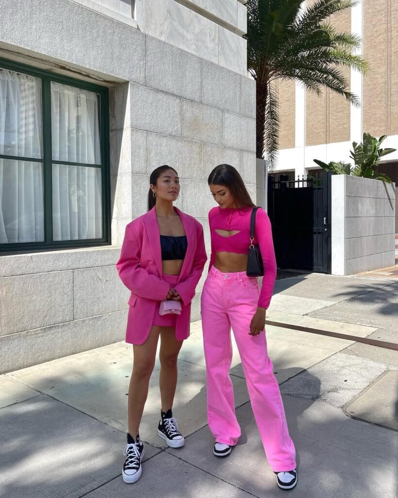 Two sporty Valentine’s outfits in hot pink—one with a blazer, crop top, shorts and sneakers; the other with a cut-out crop top, relaxed jeans, and chunky sneakers.